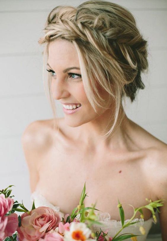 a large braided crown updo with locks down and fresh blooms tucked in is a chic and fresh hairstyle for a boho bride