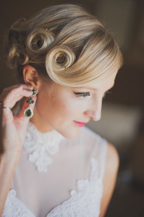 a voluminous vintage-inspired wedding updo with a twisted lower part and a large volume on top plus locks down