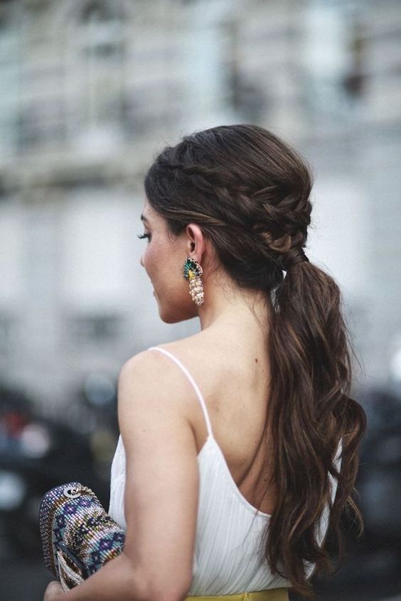 a wavy ponytail with a fishtail braid on one side and some bangs is a relaxed and casual wedding hairstyle idea